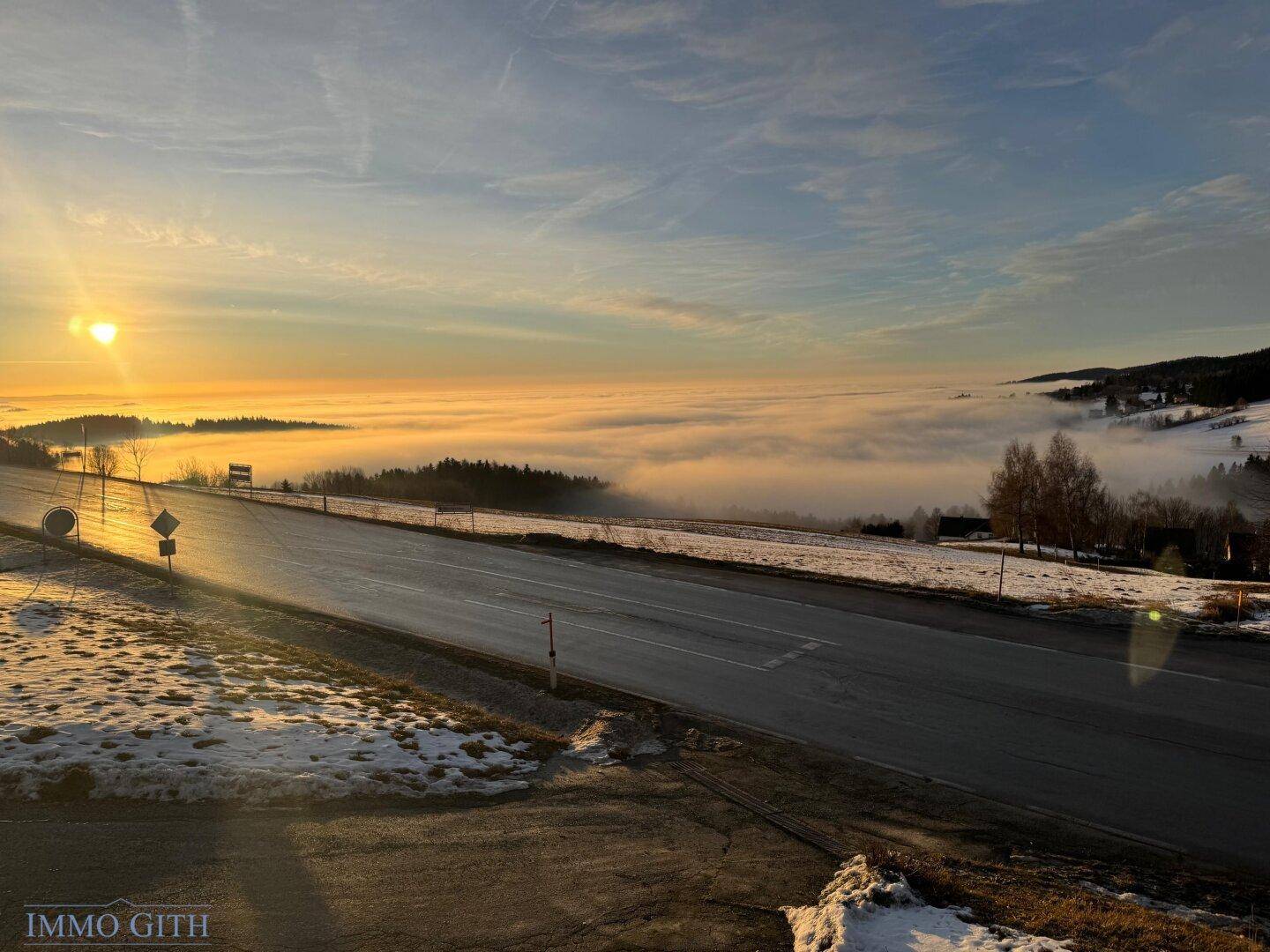 Weitläufige Landschaft bei Sonnenuntergang mit Nebel über den Tälern und einer Straße.