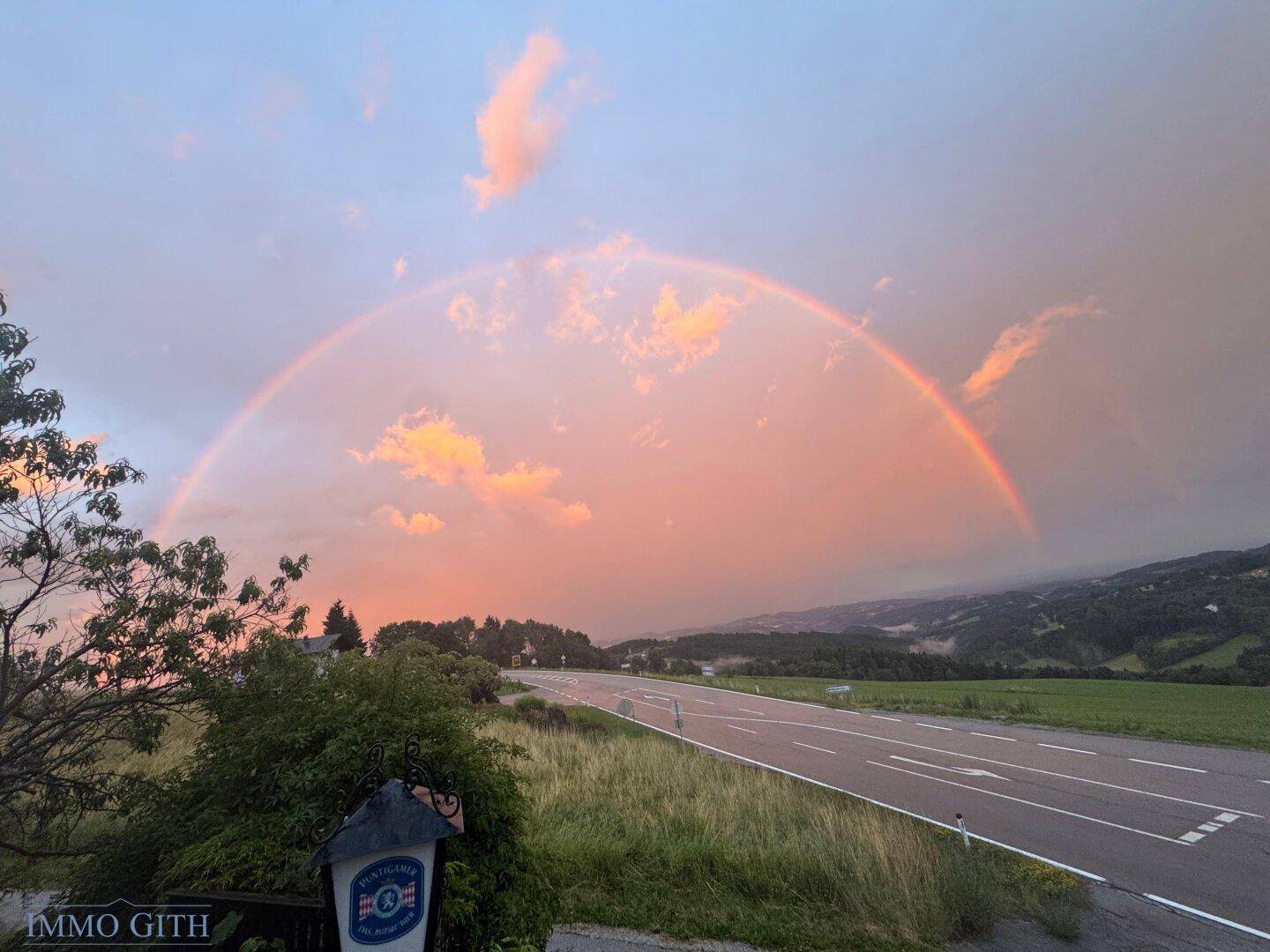 Atemberaubender Regenbogen über einer weiten Landschaft mit Straße und grünen Hügeln.