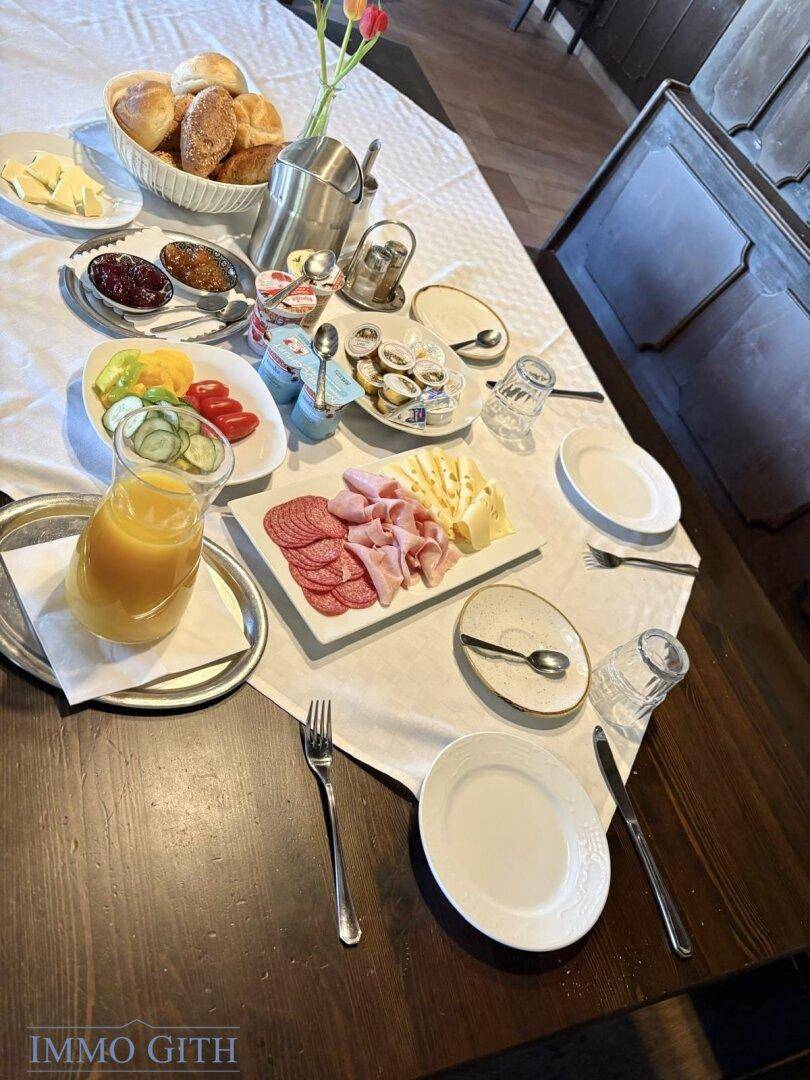 Reichhaltiges Frühstücksbuffet mit frischen Brötchen, Aufschnitt, Käse und Säften auf einem gedeckten Tisch.