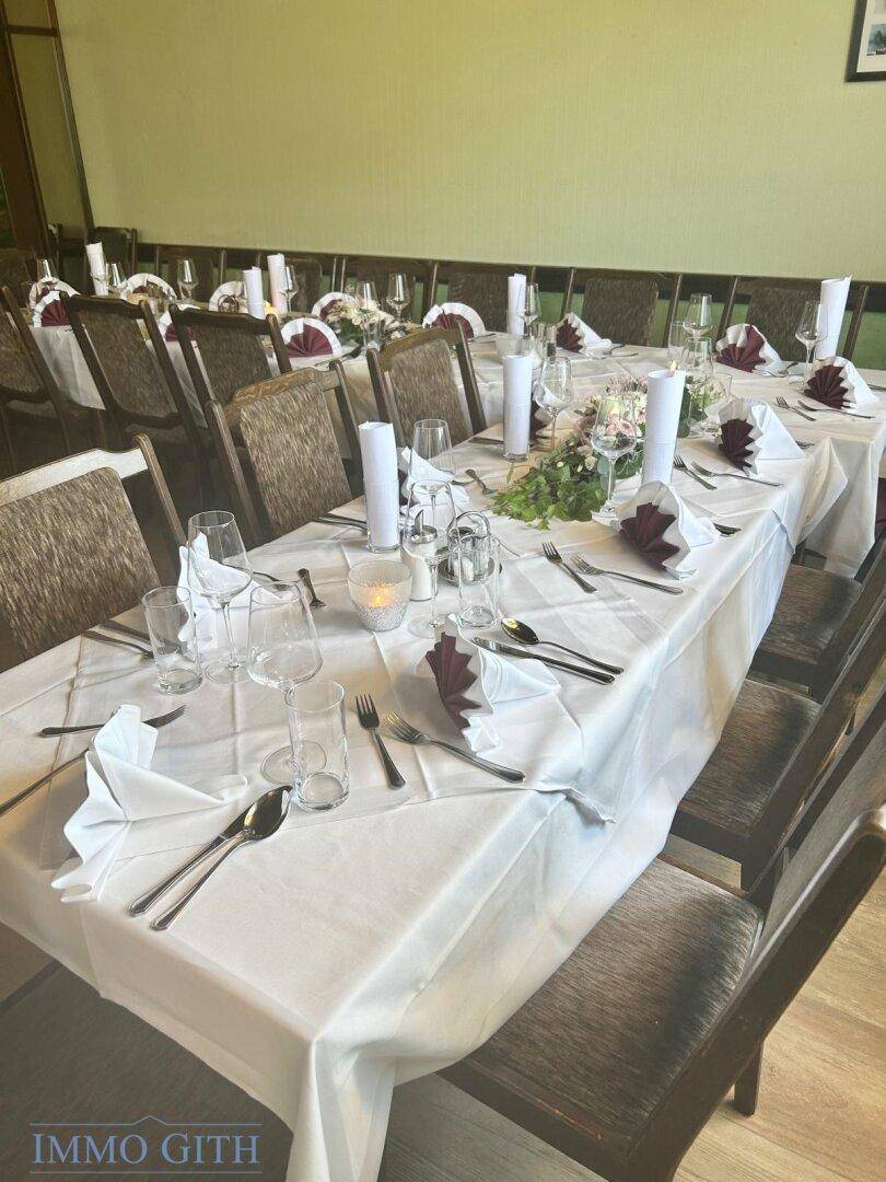 Festlich gedeckter langer Esstisch mit weißen Tischdecken, Kerzen und Servietten in einem Restaurantbereich.