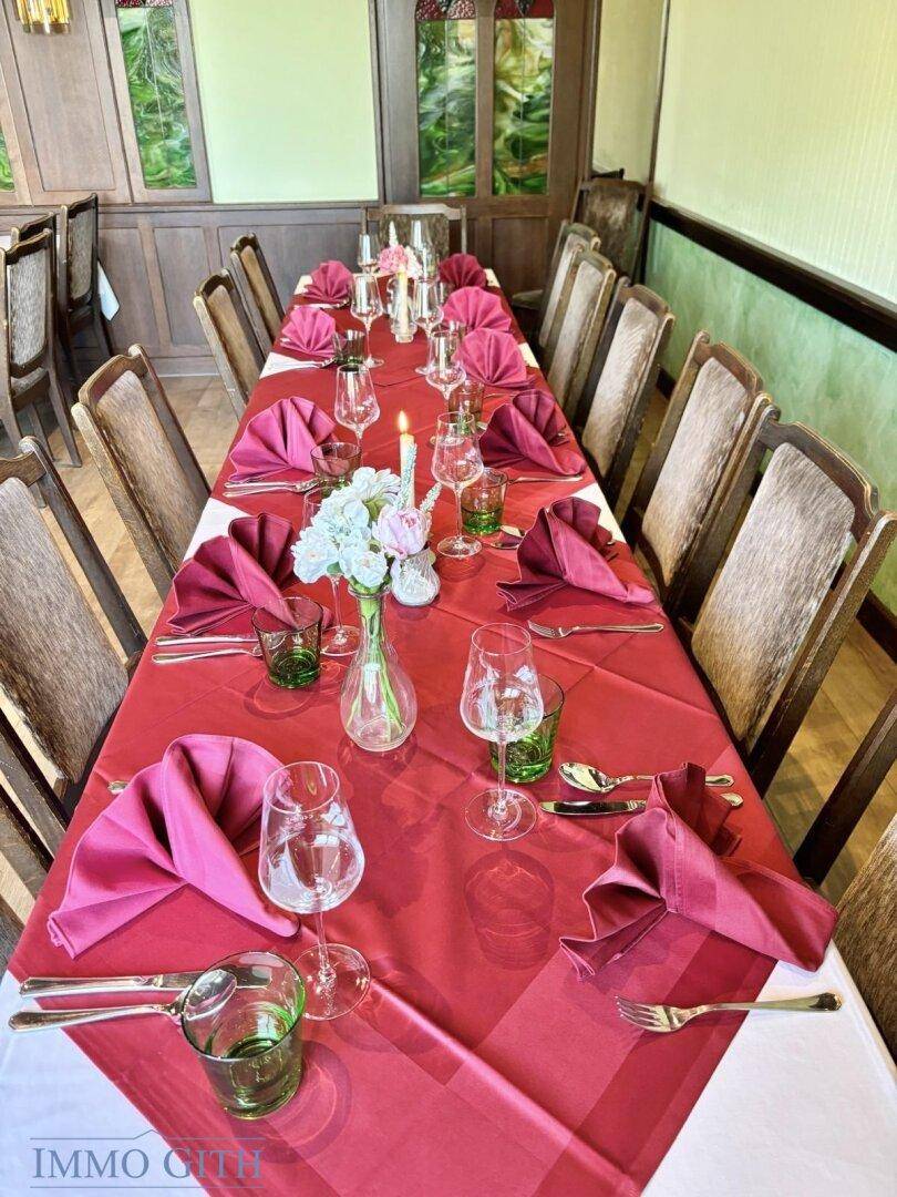 Detailansicht eines festlich gedeckten Tisches mit roten Servietten, grünen Gläsern und Blumenarrangements.