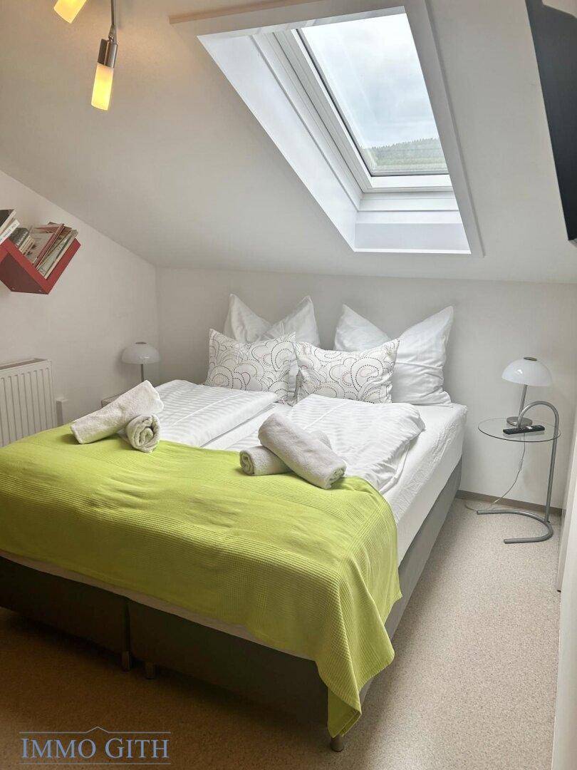 Gemütliches Schlafzimmer mit Doppelbett, Dachfenster und schräger Decke, hell und freundlich eingerichtet.