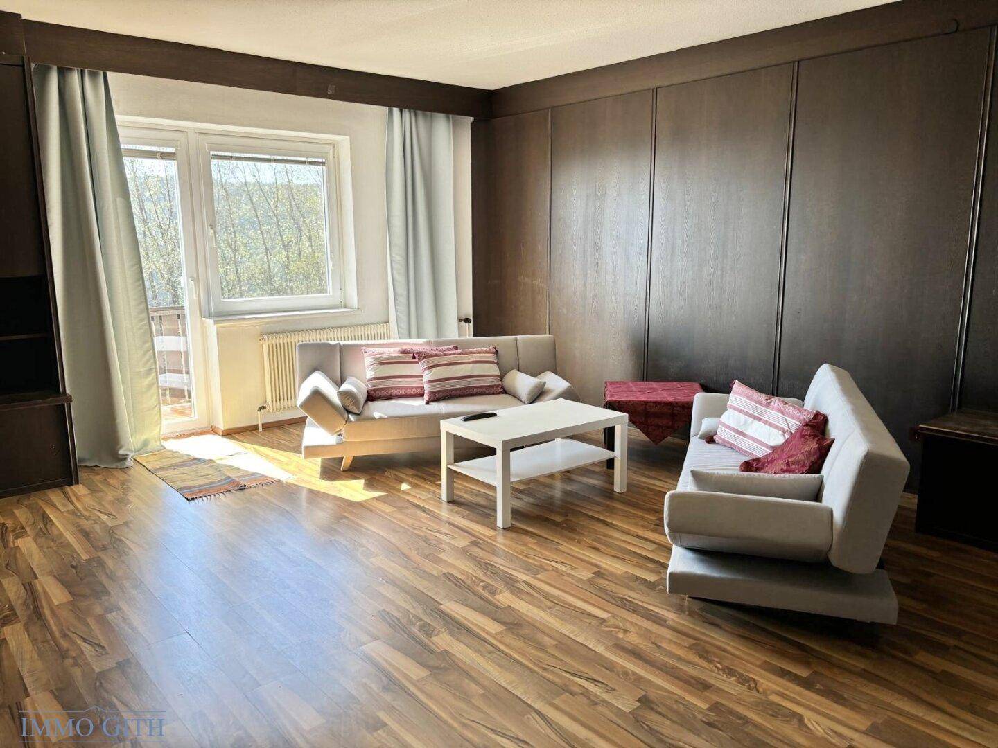 Helles Wohnzimmer mit Holzboden, zwei bequemen Sofas und einem Fenster mit Blick ins Grüne.
