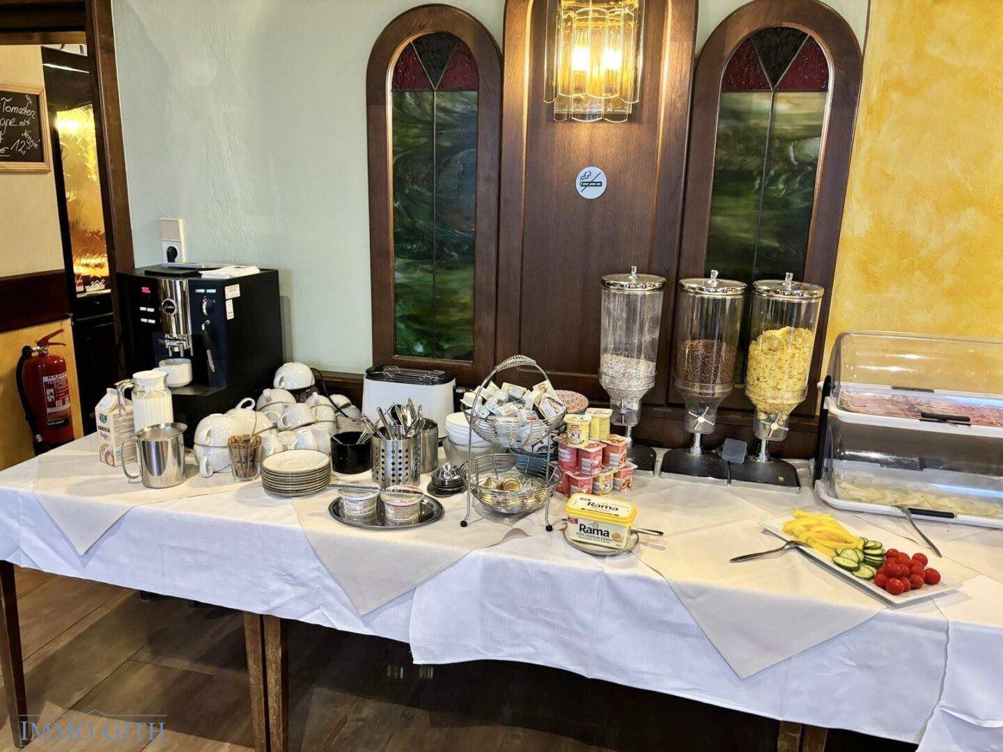 Umfangreiches Frühstücksbuffet mit Kaffeemaschine, Müsli, Aufstrichen und frischen Früchten in einem Speisesaal.