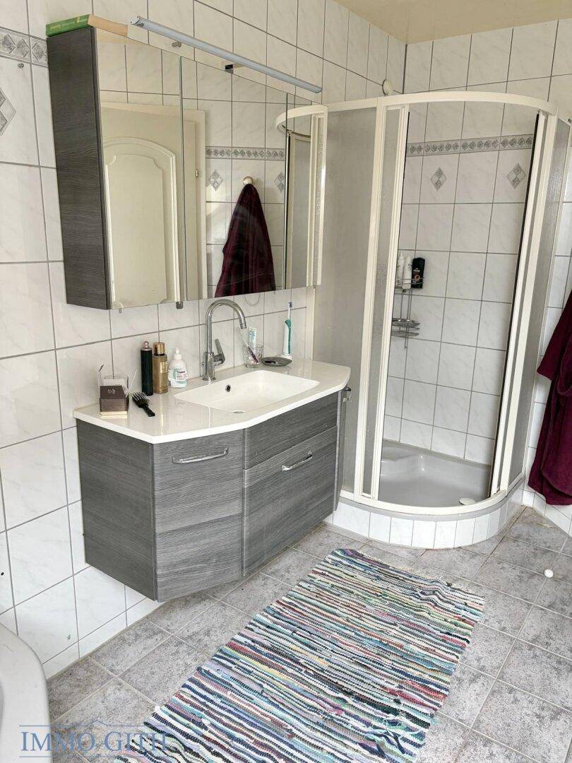 Modernes Badezimmer mit Waschtisch, Spiegelschrank und einer Eckdusche, komplett gefliest.