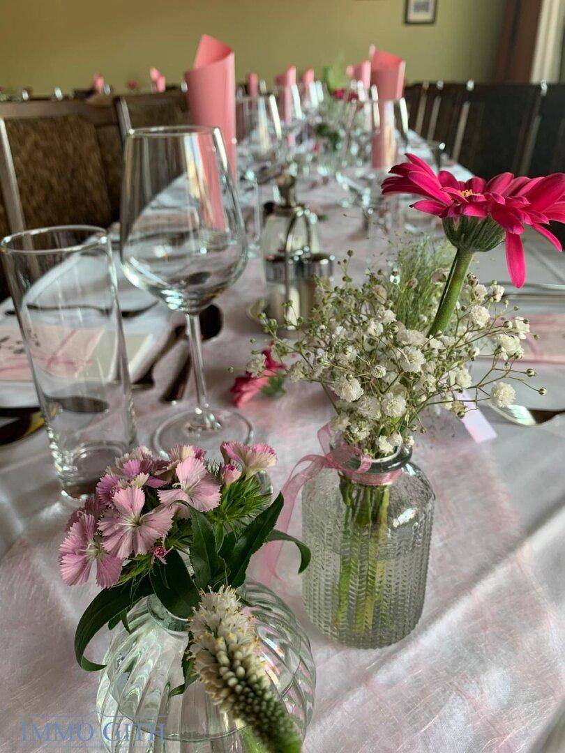 Nahaufnahme eines festlich gedeckten Tisches mit zarten rosa Blumenarrangements und Gläsern.