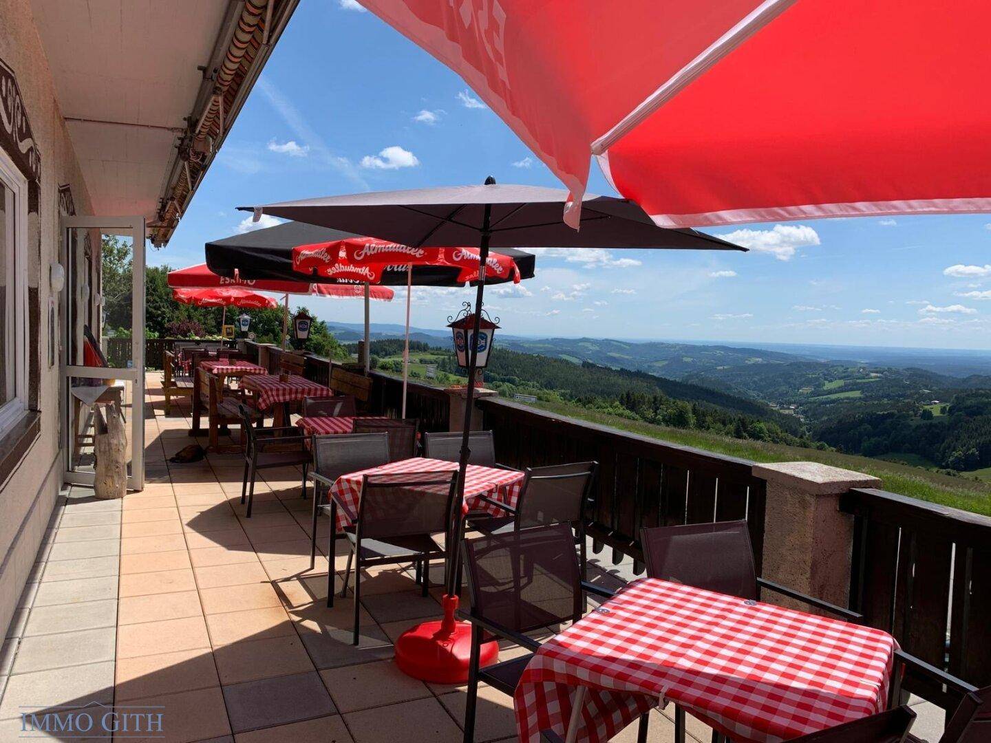 Große Außenterrasse mit Tischen, Stühlen und roten Sonnenschirmen, die einen weiten Panoramablick bietet.