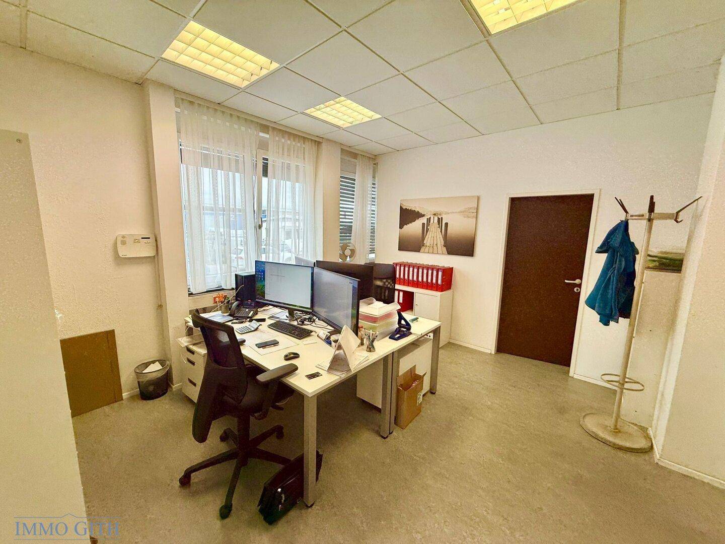 Modern eingerichtetes Büro mit zwei Computermonitoren, einem Schreibtisch und einem Bürostuhl.