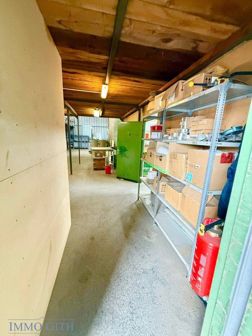Langer, schmaler Lagerbereich mit Regalen voller Kartons und einem Feuerlöscher an der Seite.