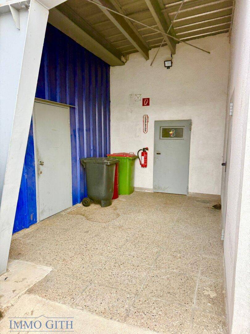 Kleiner Flur oder Abstellbereich mit zwei Türen, Mülleimern und einem Feuerlöscher an der Wand.