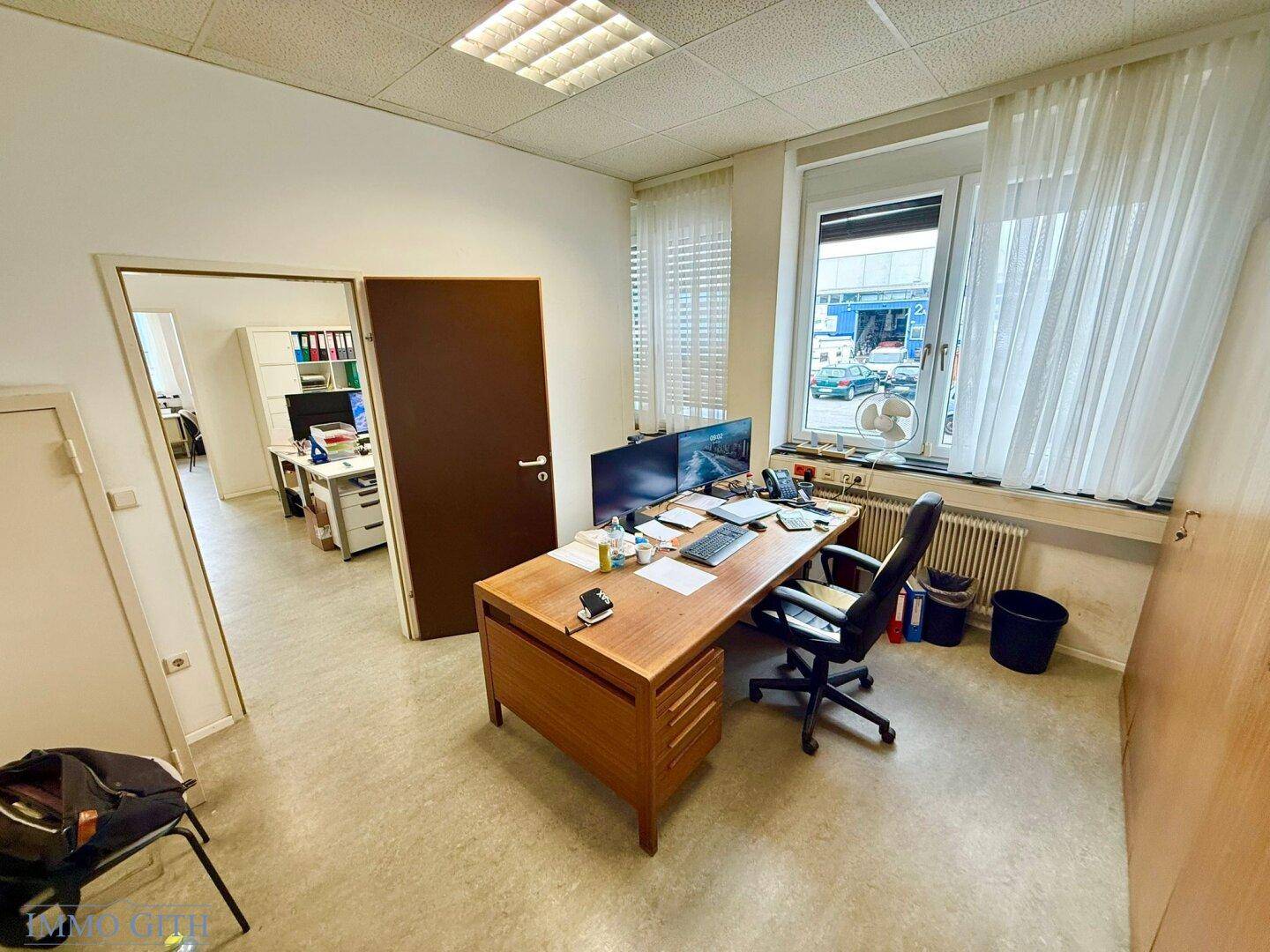 Büro mit einem Holzschreibtisch, Bürostuhl und einem Fenster, das den Blick nach draußen freigibt.