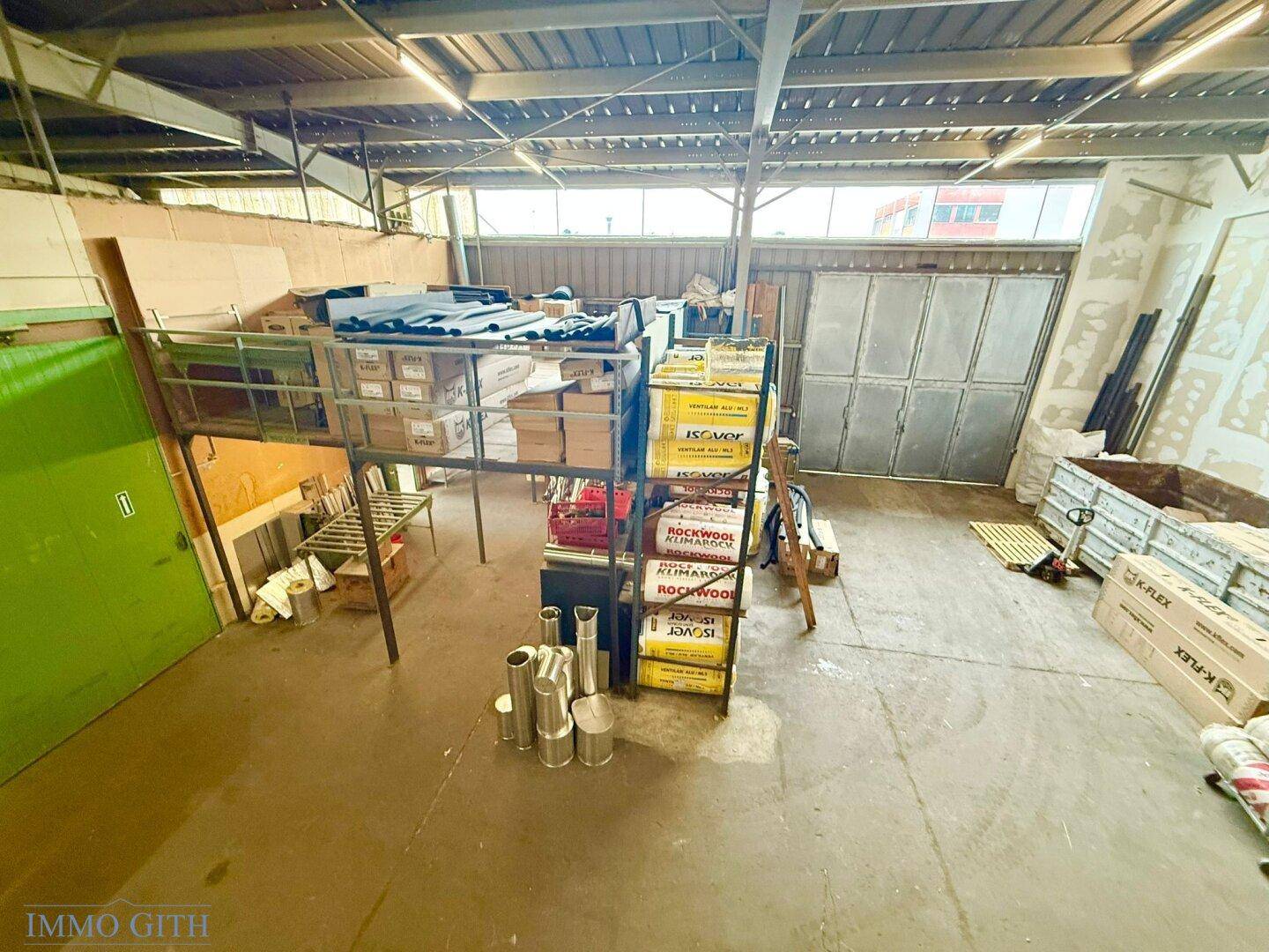 Lagerhalle mit Zwischengeschoss, gestapelten Isolationsmaterialien und einer großen Tür im Hintergrund.