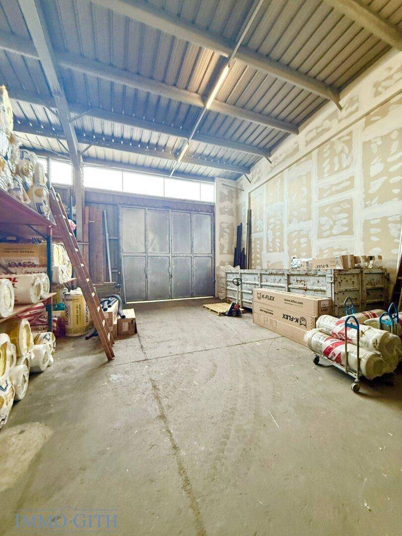 Erdgeschoss einer Lagerhalle mit großer Rolltür, gestapelten Materialien und unverputzten Wänden.