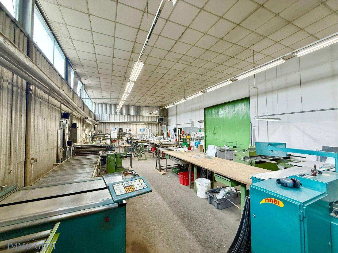 Werkstattraum mit verschiedenen Maschinen, langen Arbeitstischen und industrieller Beleuchtung für Produktion.