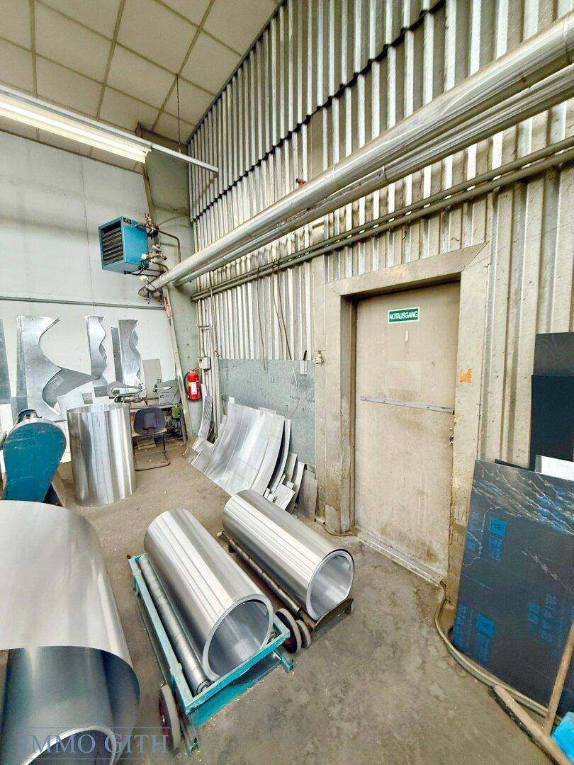 Innenansicht eines Lagerbereichs mit gestapelten Metallplatten, einer Tür und sichtbaren Rohren an der Decke.