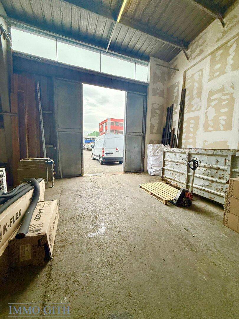 Innenansicht eines Lagerraums mit Blick durch große Tore auf den Außenbereich und einen weißen Lieferwagen.