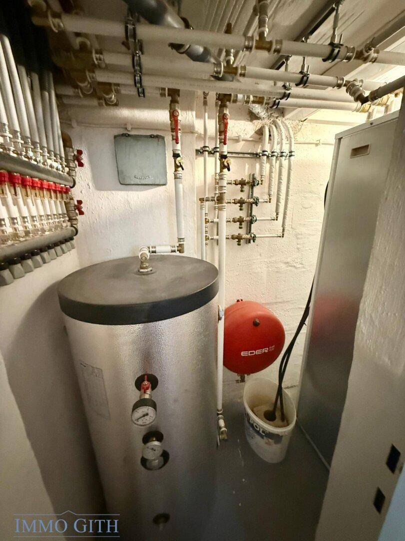Heizungsraum im Keller mit Warmwasserspeicher und komplexen Rohrleitungen, gut organisiert.