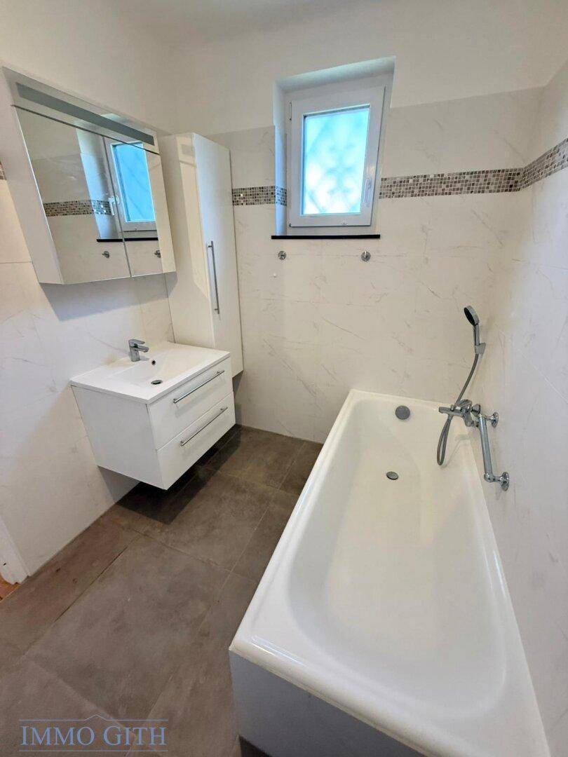 Modernes Badezimmer mit Badewanne, Waschbecken und Spiegelschrank, ausgestattet mit Fenster.