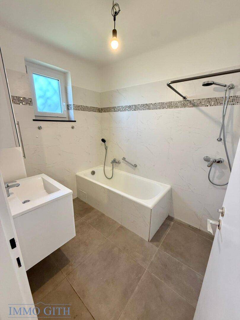 Helles Badezimmer mit Badewanne, Duschvorrichtung und modernem Waschbecken, in gutem Zustand.