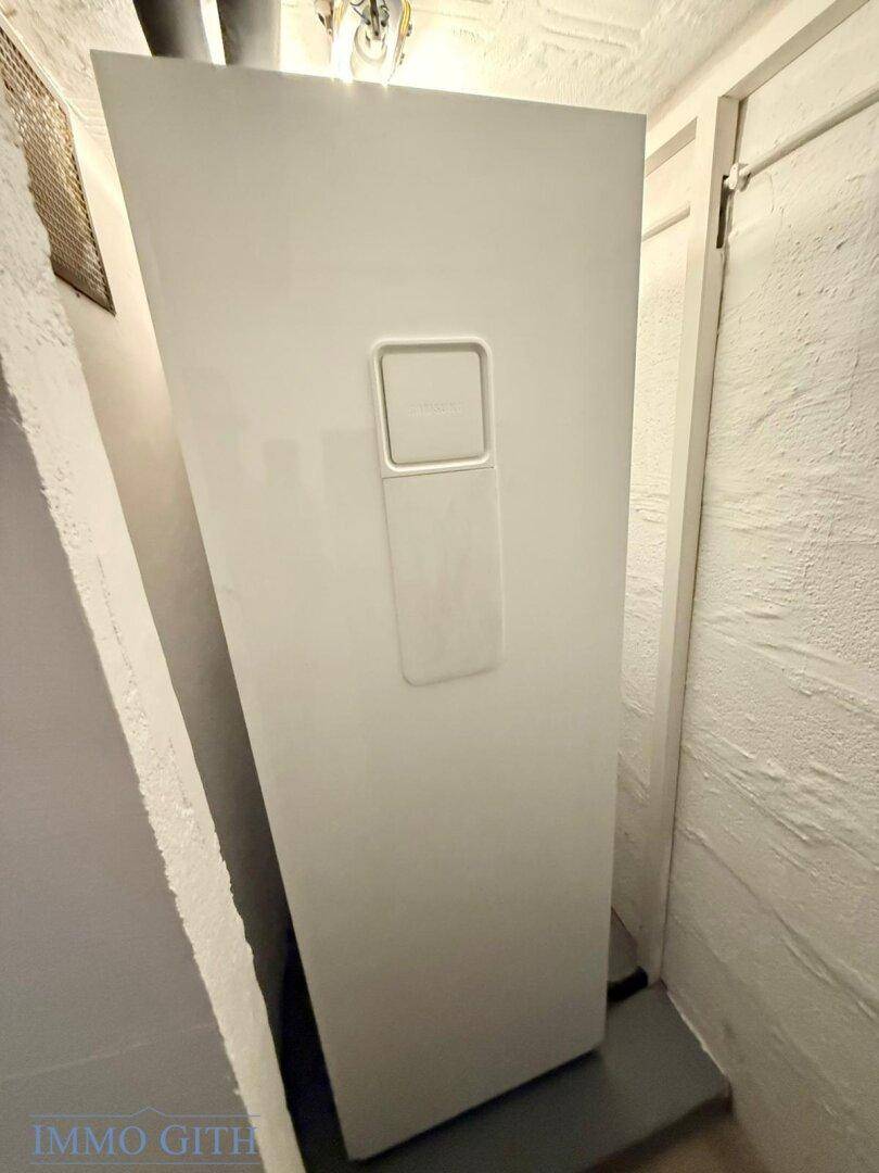 Geräumiger Hauswirtschaftsraum mit großem weißen Gerät und Lüftungsgitter, im Keller gelegen.