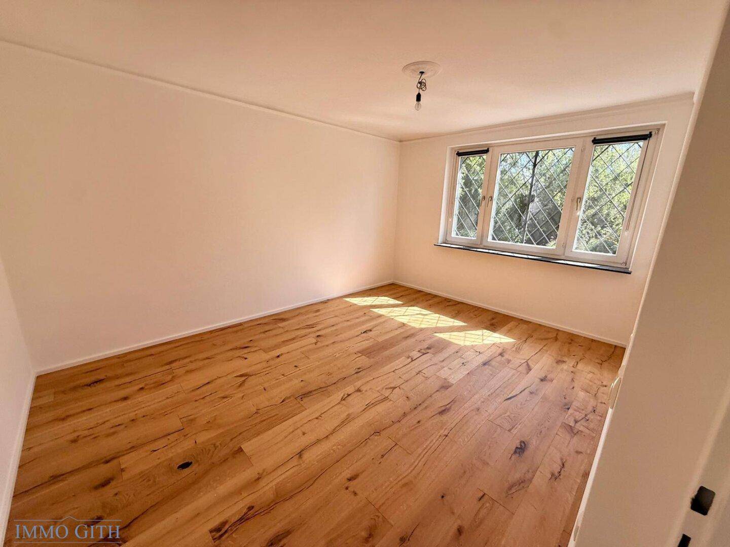 Freundliches Zimmer mit Holzboden und viel Tageslicht durch das Fenster, bereit zum Einzug.