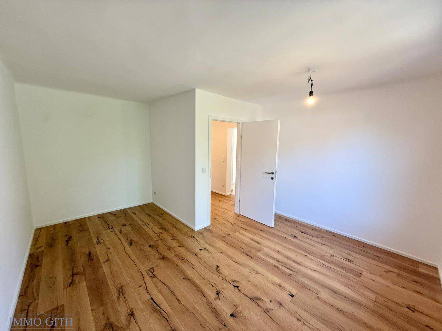 Leeres Zimmer mit Holzboden und Zugang zu einem weiteren Bereich, bietet flexible Nutzungsmöglichkeiten.