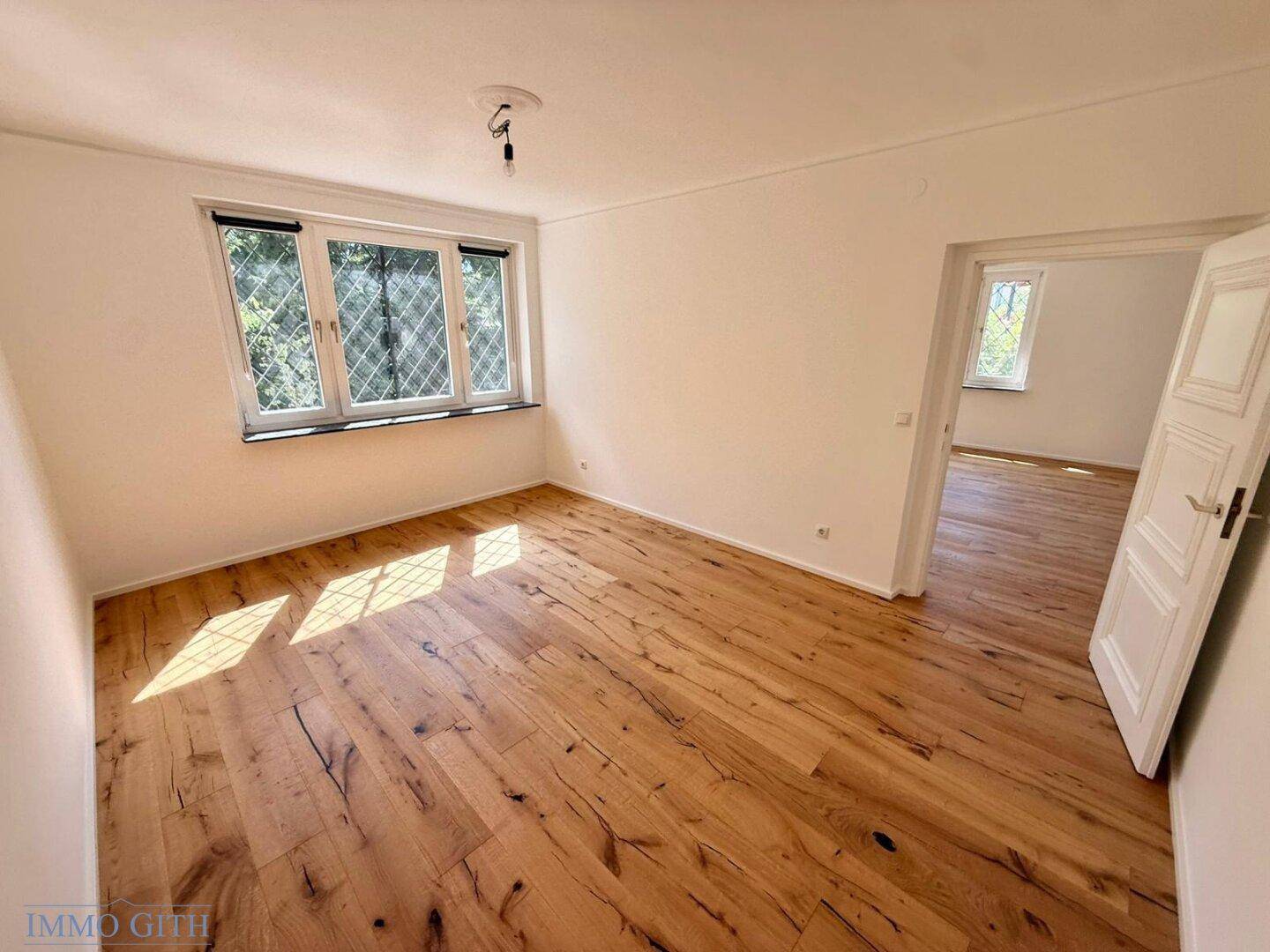 Geräumiges Wohnzimmer mit Holzboden und Blick in einen weiteren, hellen Raum des Hauses.