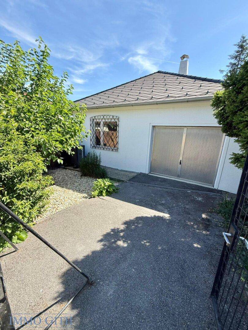 Seitenansicht des Hauses mit Einfahrt zur Garage und grünem Bewuchs unter blauem Himmel.