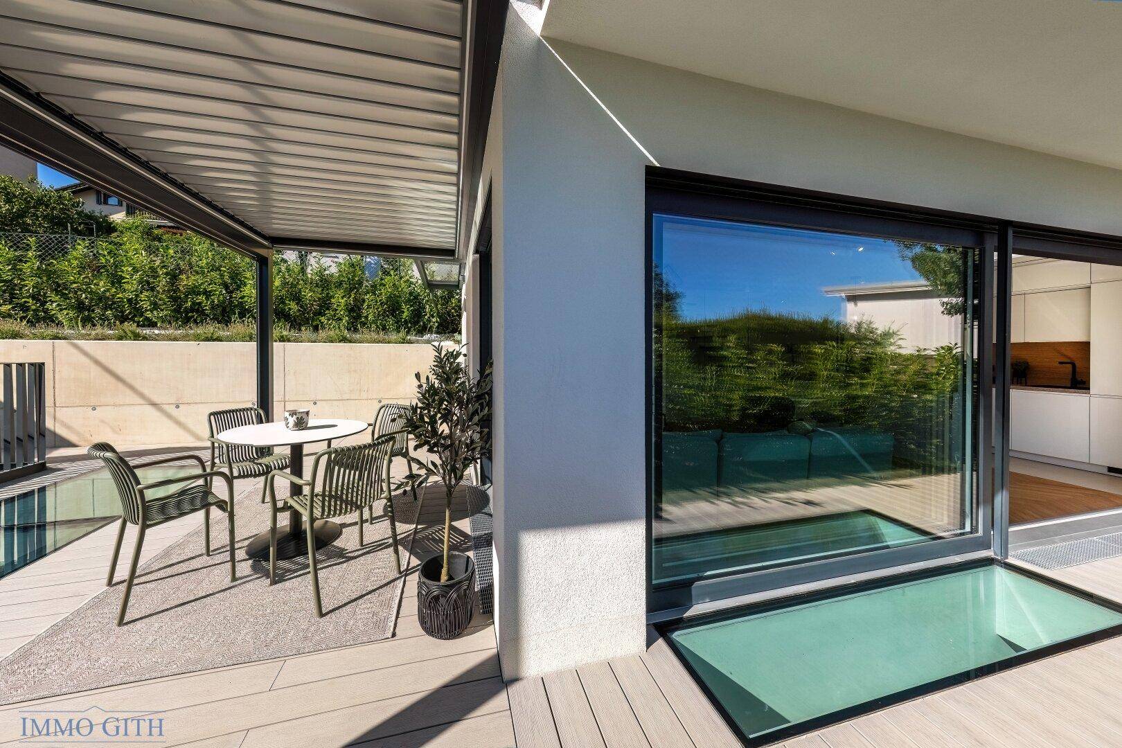 Überdachte Terrasse mit Sitzgelegenheiten und großen Glasfronten, die den Innenraum mit dem Außenbereich verbinden.