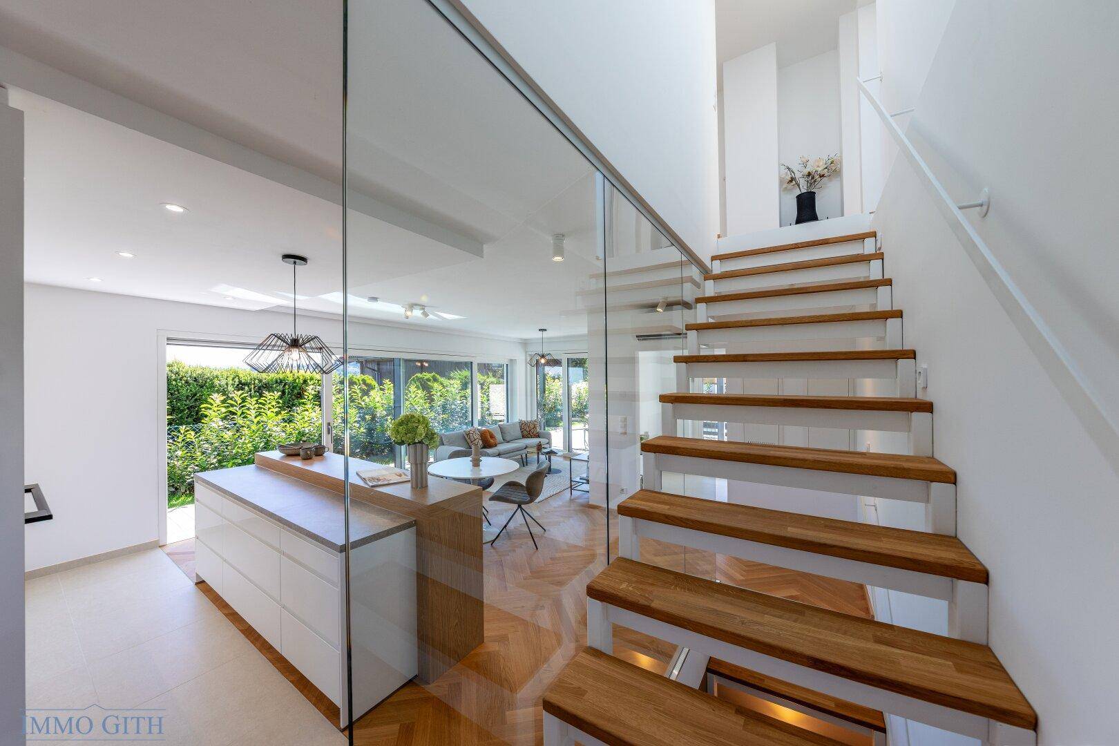 Moderner Eingangsbereich mit offener Holztreppe, Glasgeländer und Blick in den Wohnbereich.