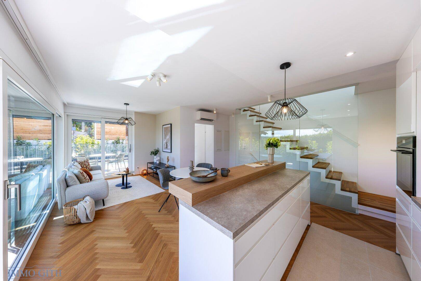 Geräumiger offener Wohn-Essbereich mit moderner Küche, Glas-Treppe und Zugang zur Terrasse.