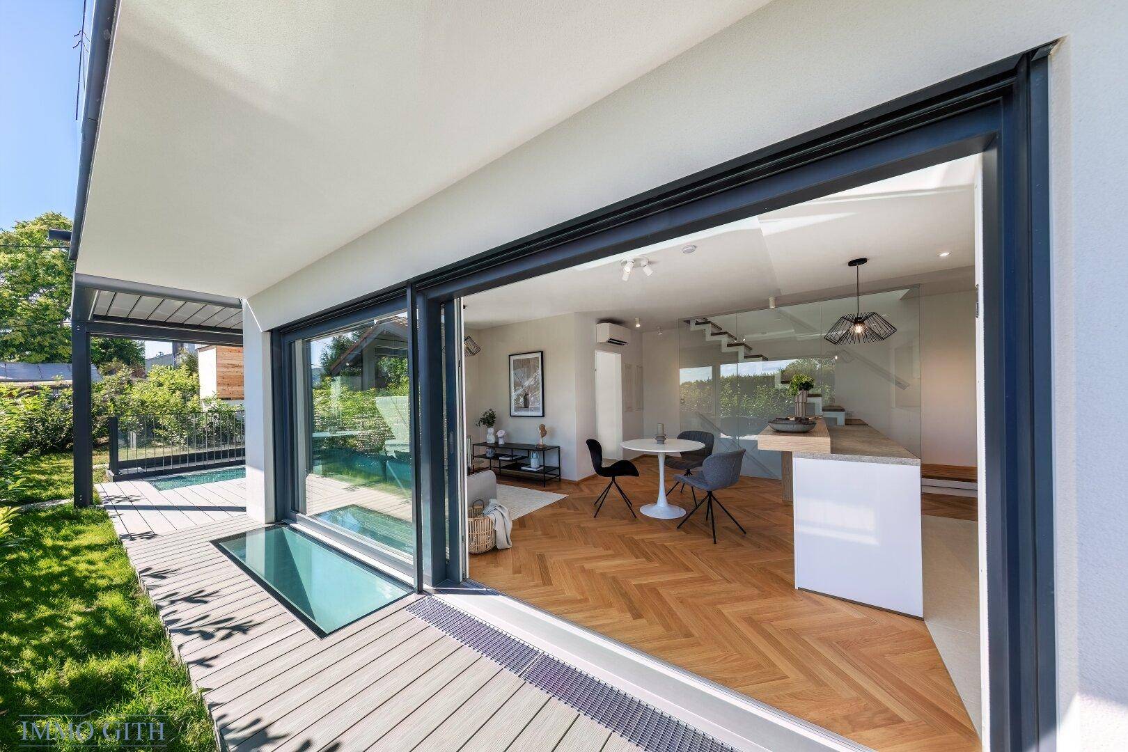 Große Schiebetüren öffnen den Wohnbereich zur Terrasse mit Rasenfläche und Glasboden.