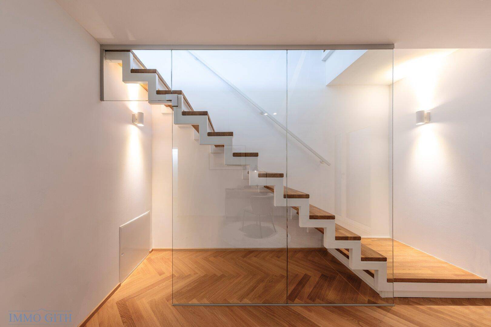 Elegante moderne Treppe mit Holzstufen und Glasgeländer, stilvoll beleuchtet.