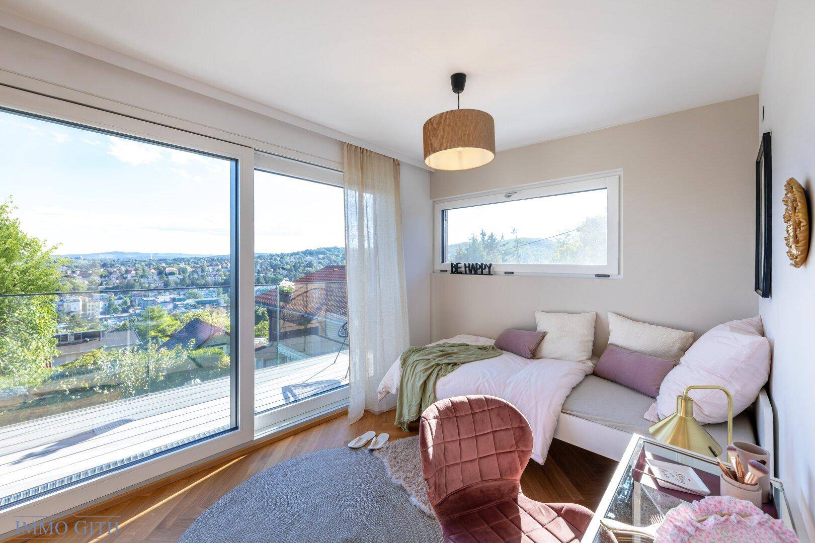 Helles Schlafzimmer mit Tagesbett, Schreibtisch und Panoramafenstern, die einen weiten Ausblick bieten.