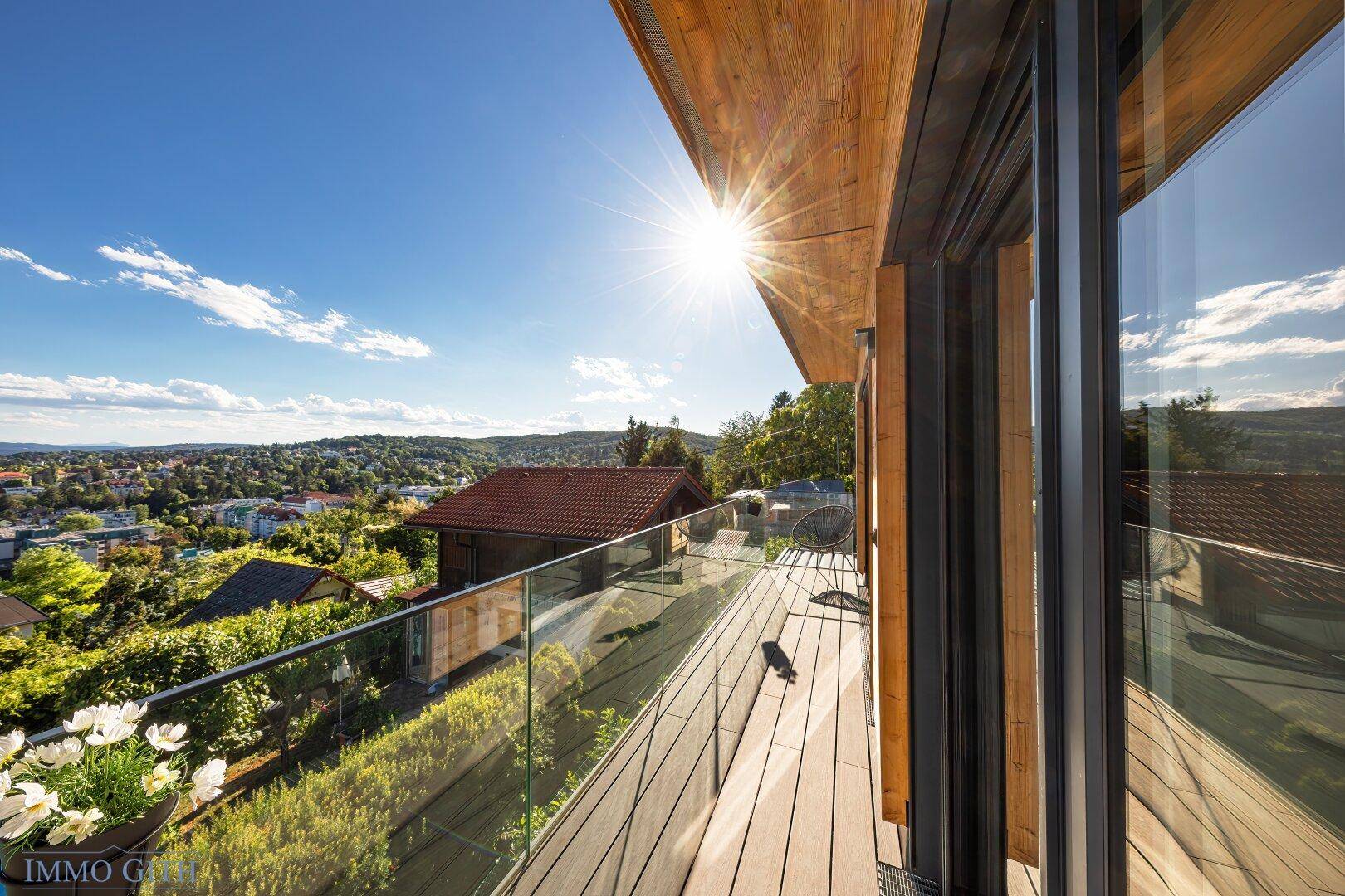 Sonniger Balkon mit Glasgeländer und weitem Panoramablick über die Stadt und die grüne Landschaft.