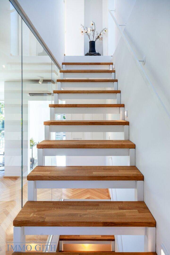 Elegante Holztreppe mit Glasgeländer in einem hellen, modernen Eingangsbereich.