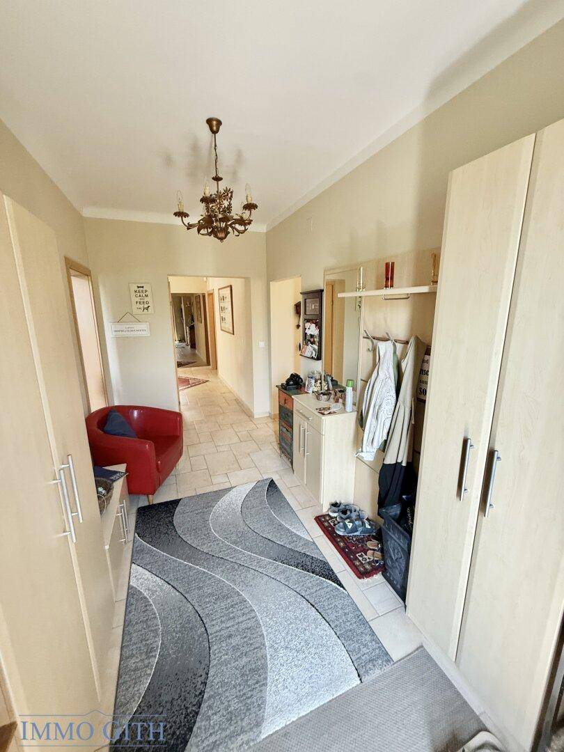 Geräumiger Flur mit Fliesenboden, Garderobe und einem roten Sessel.
