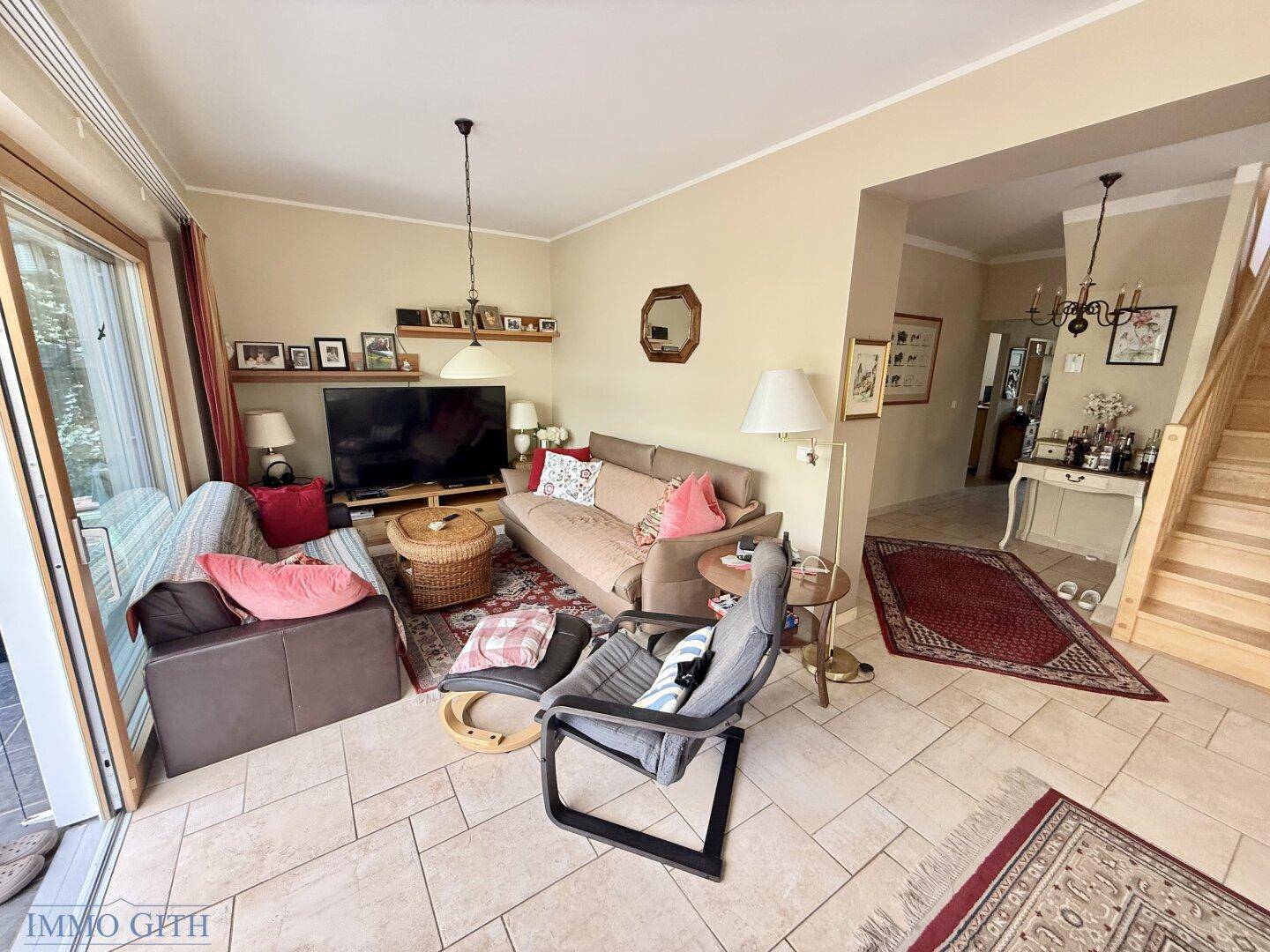 Helles Wohnzimmer mit Sofa, Fernseher und großem Schiebetürzugang zur Terrasse.