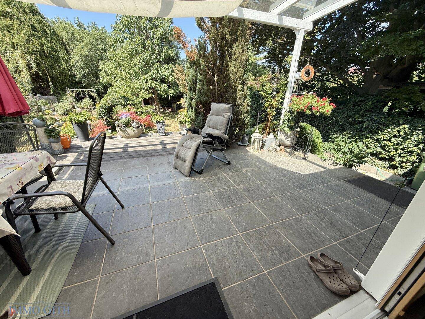 Geräumige geflieste Terrasse mit Gartenmöbeln und Sonnenschutz.