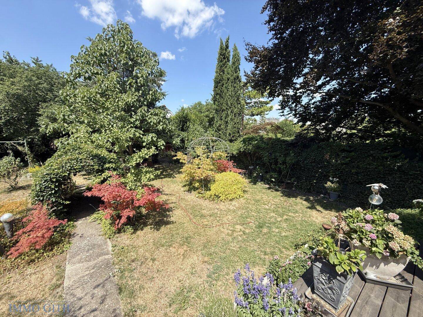 Weitläufiger Garten mit üppiger Vegetation, Bäumen und einem sonnigen Rasenbereich.