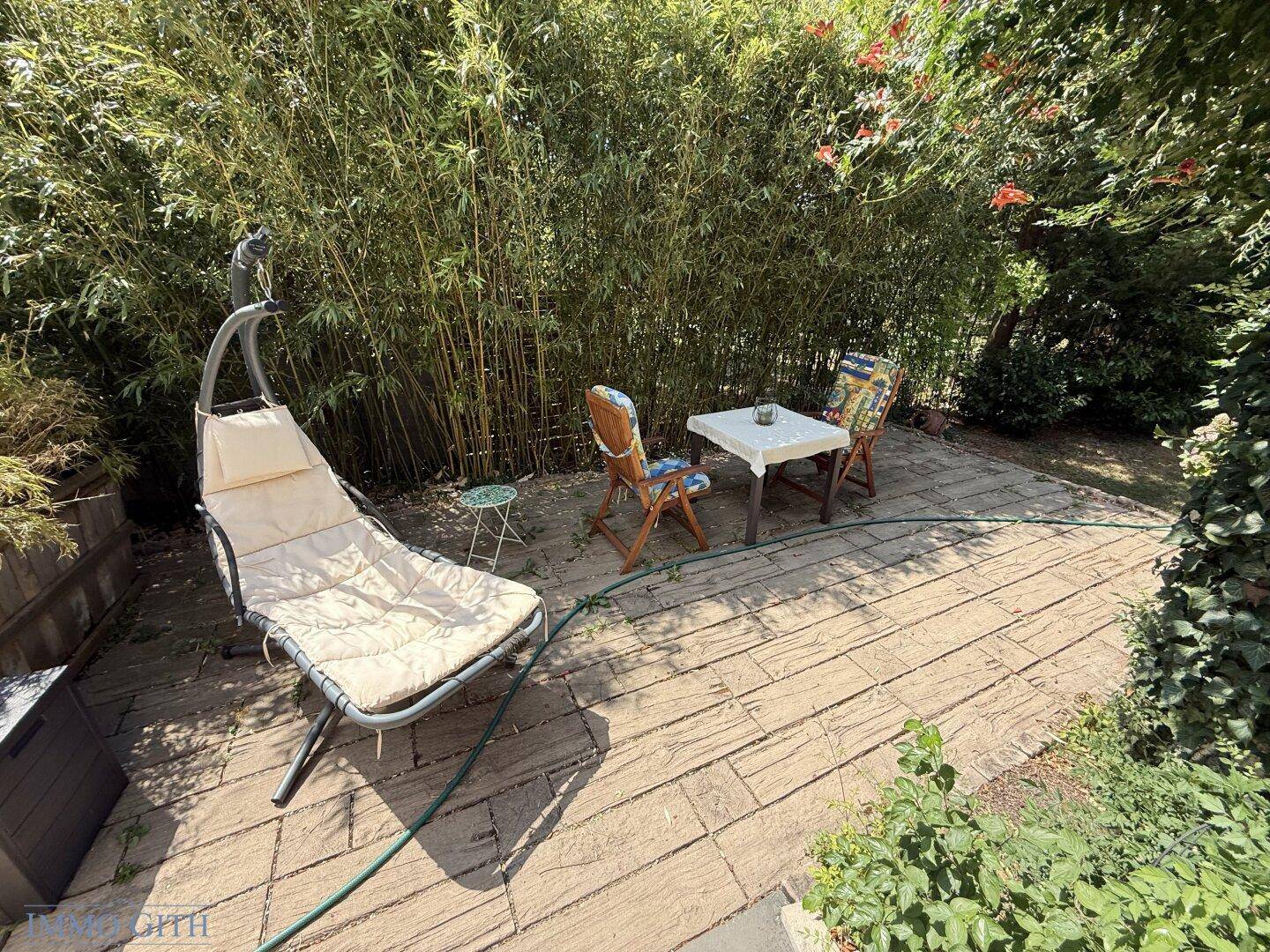 Gemütliche gepflasterte Terrasse mit Sitzgelegenheiten und üppiger Bambusbepflanzung im Gartenbereich.