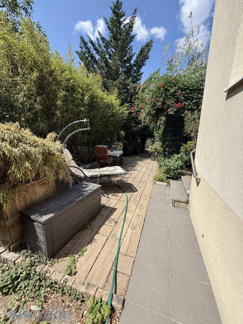 Gepflasterter Gartenweg führt zu einer kleinen Terrasse mit Sitzgelegenheiten und üppiger Bepflanzung.