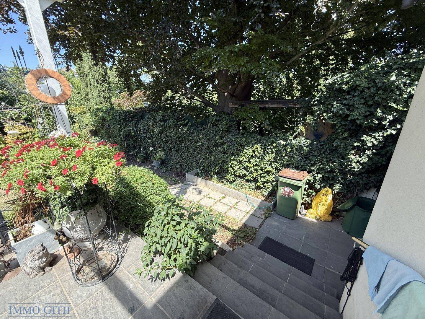 Gefliester Eingangsbereich mit Treppe und Blick auf den grünen, bewachsenen Garten.