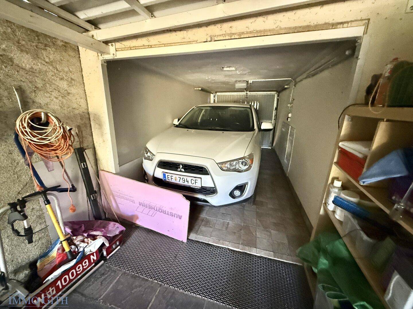 Auto in der Garage geparkt, umgeben von verschiedenen Lagergegenständen und Regalen.