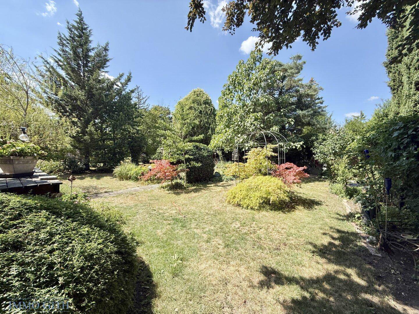 Großer, gepflegter Garten mit vielfältiger Bepflanzung, Bäumen und Sträuchern unter blauem Himmel.