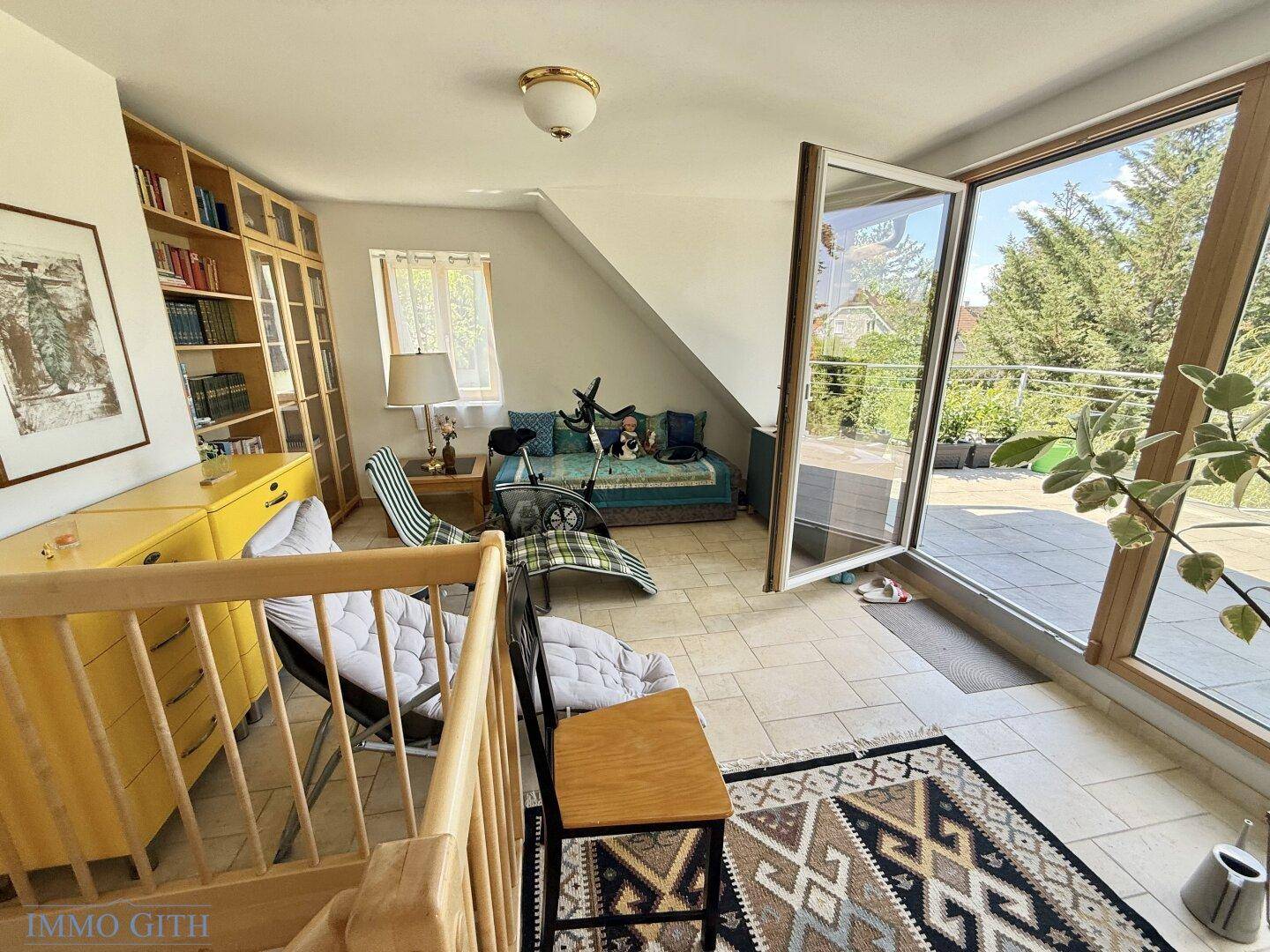 Helles Zimmer mit Dachschräge, großen Fenstern und Zugang zu einer sonnigen Terrasse.