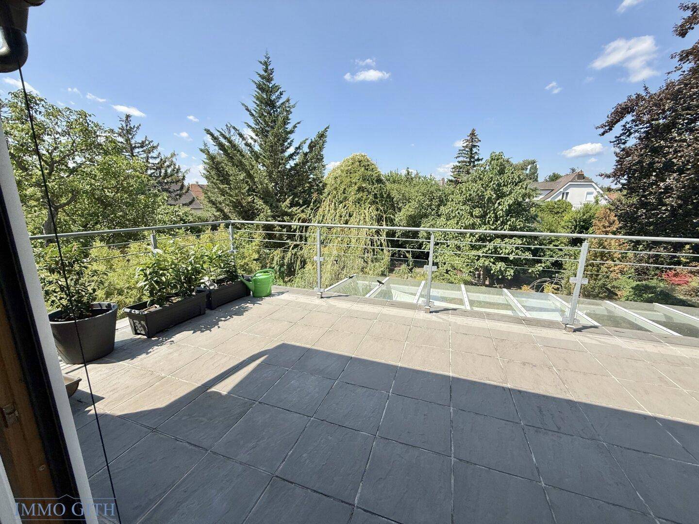 Geräumige Dachterrasse mit Fliesenboden, Metallgeländer und weitem Blick ins Grüne.