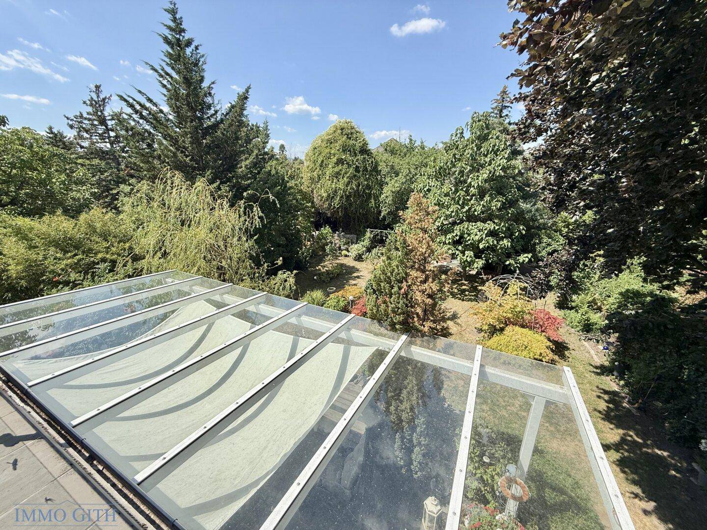 Blick von der Dachterrasse auf ein Glasdach und den darunterliegenden grünen Garten.