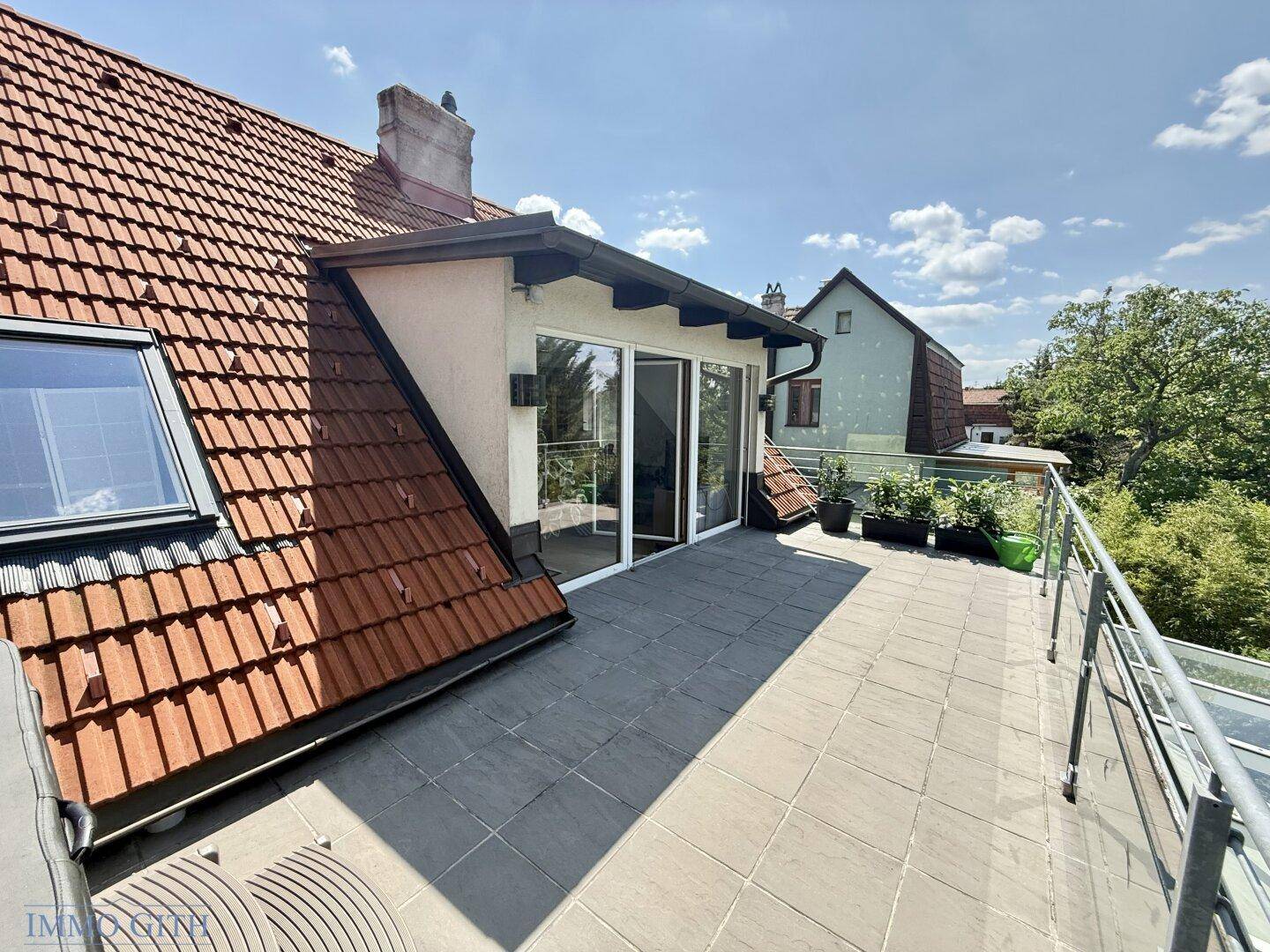 Weitläufige Dachterrasse mit Fliesenboden, Blick auf das Ziegeldach und die Umgebung.