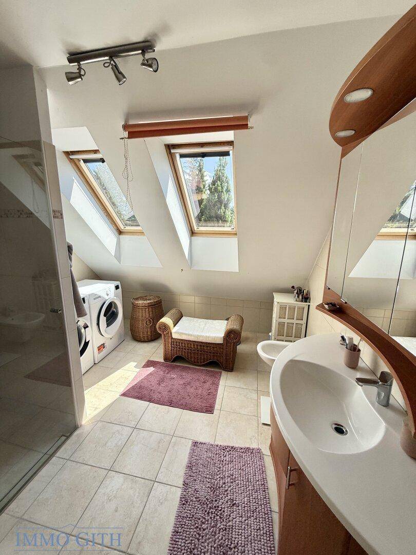 Helles Badezimmer mit Dachschräge, Dachfenstern, Waschbecken, Bidet und Waschmaschine.